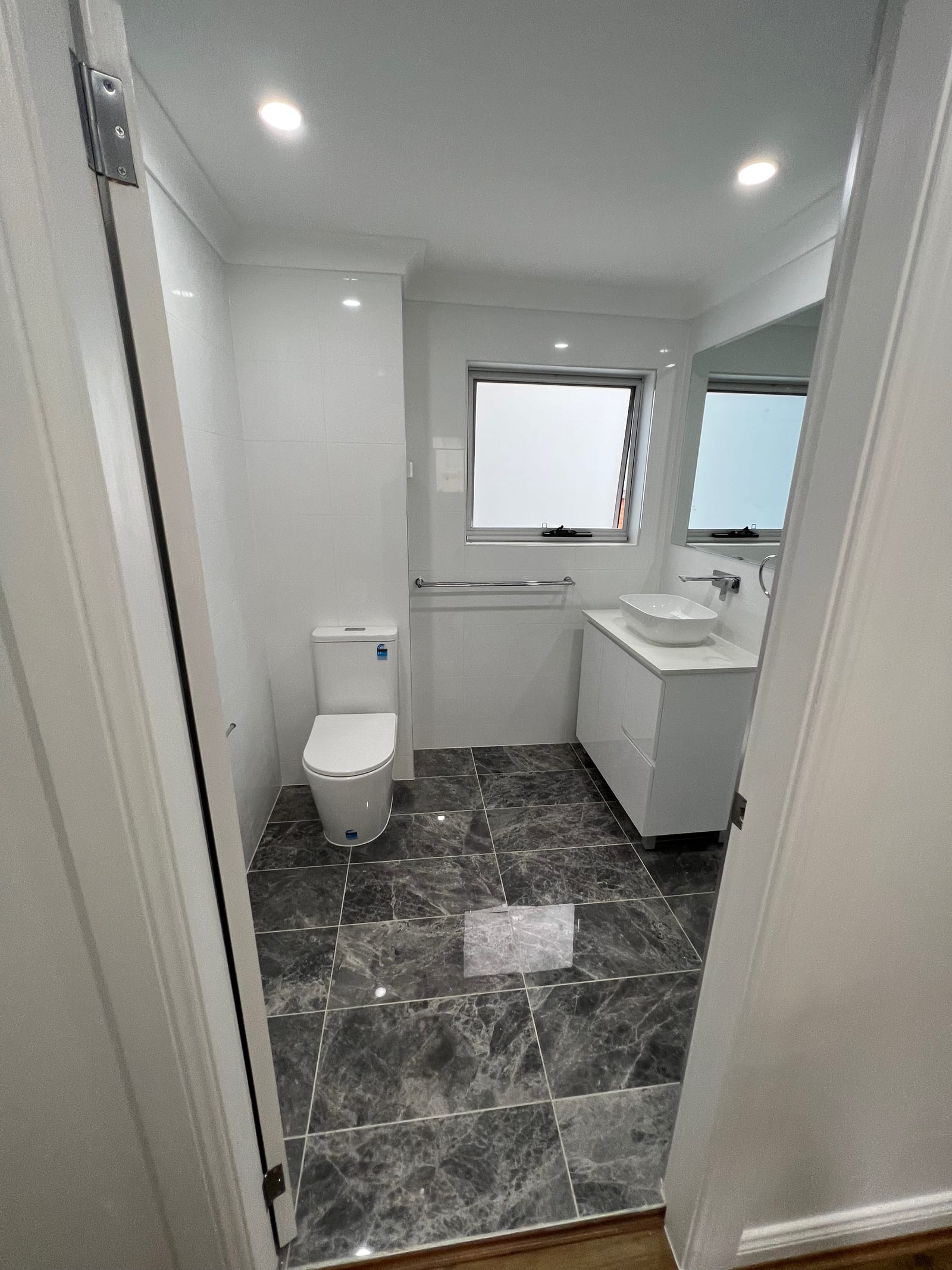 A finished bathroom — dark stone-look floor tiles, an above-counter basin on a stone-top vanity and wall-mounted tapware