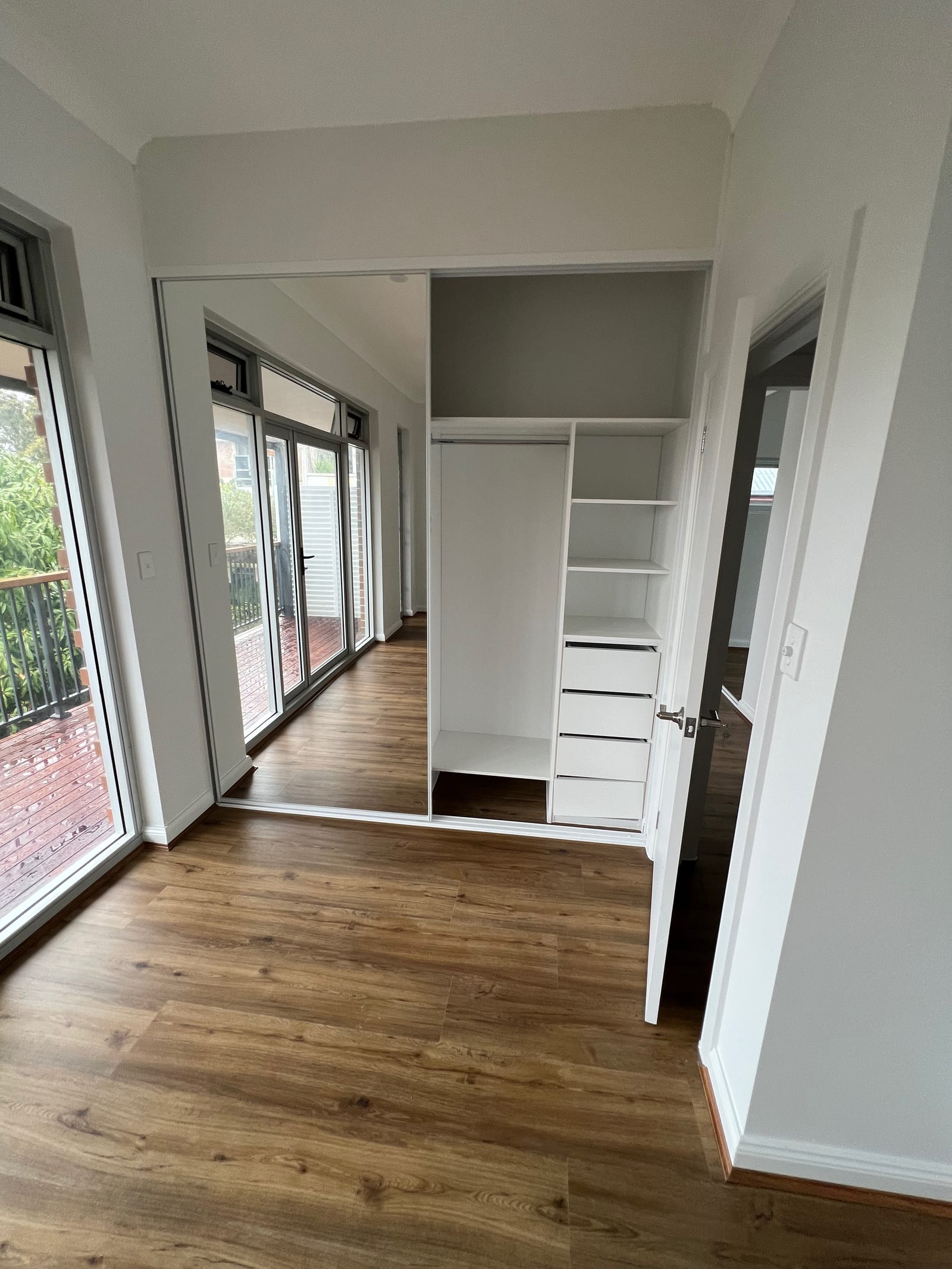 A bedroom with a built-in wardrobe — mirrored sliding doors, open hanging space, shelving and drawers