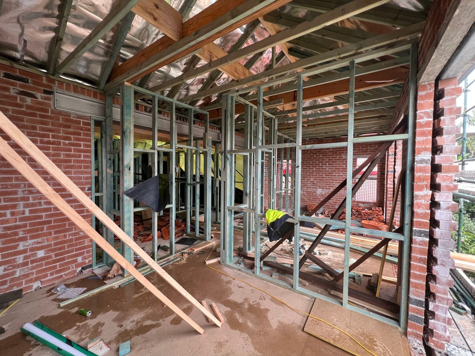 During the build — timber stud-frame partition walls inside the new upper level, with salvaged terracotta roof tiles stacked against the retained original brickwork