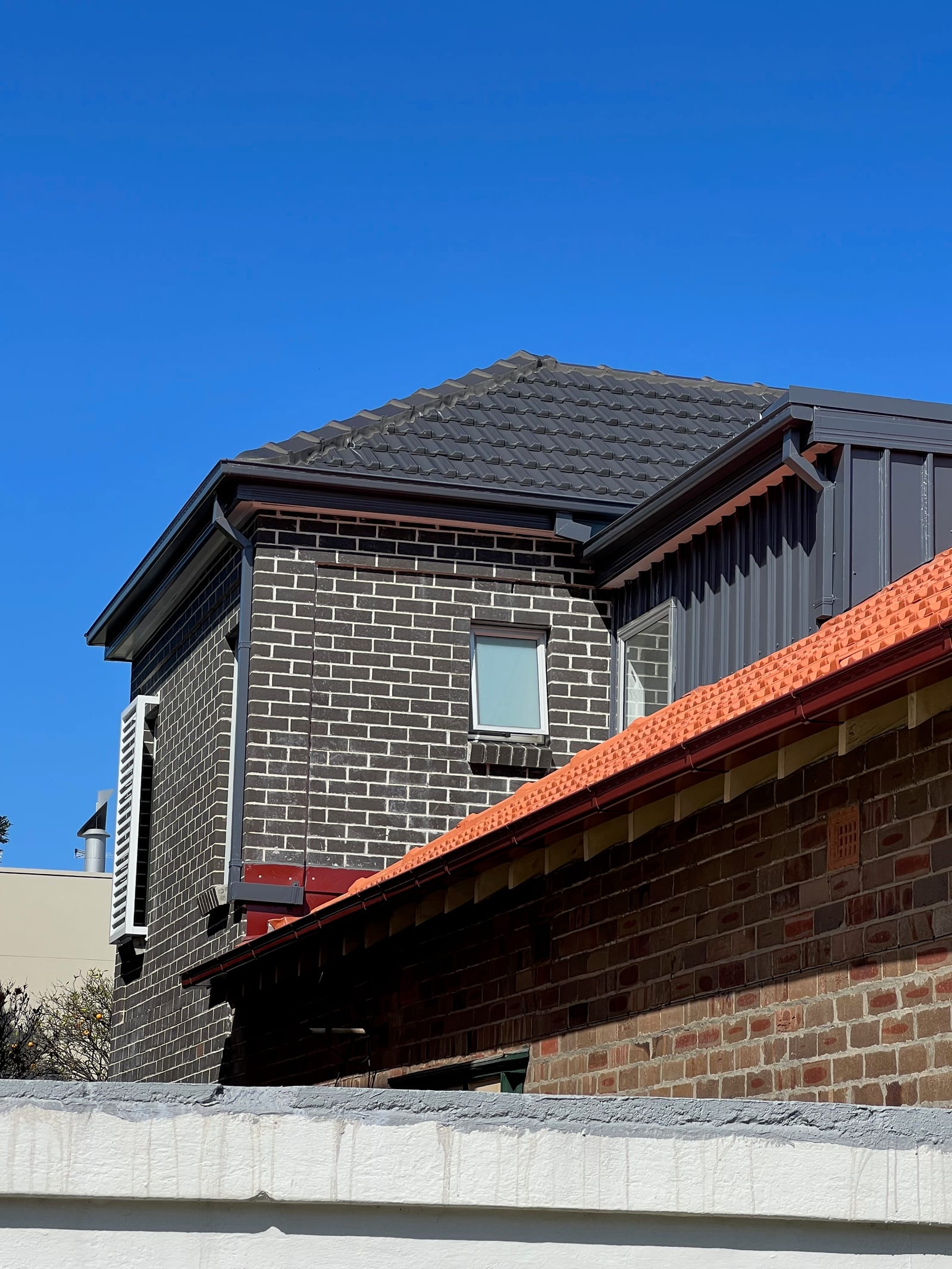 The completed upper storey seen from the side — charcoal brick and a matching dark tiled hip roof above the original terracotta roofline