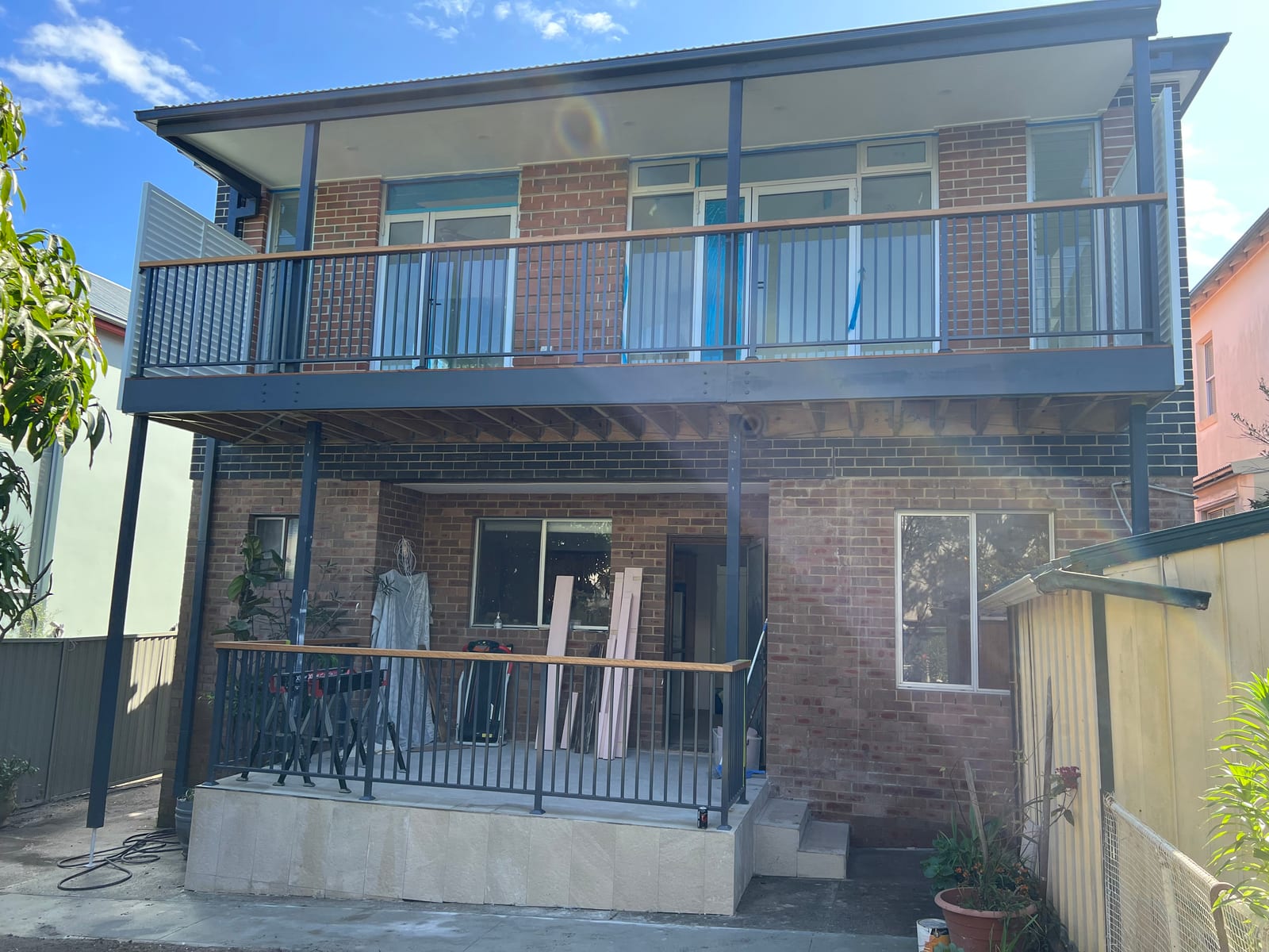 The completed rear of the Bronte home — a new upper storey in matching brick sits over the original ground floor, with a new steel-balustraded balcony on posts shading a lower-level patio
