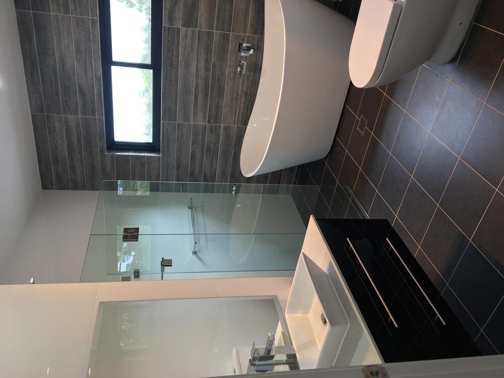 Main bathroom with a freestanding bath, frameless shower screen and dark feature tiling