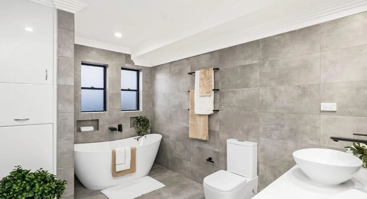 A bathroom with a freestanding bath, twin windows and full-height tiling.