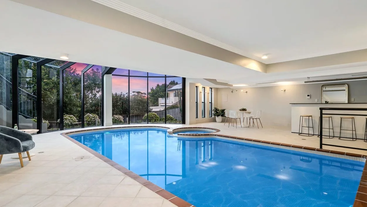 After — The new indoor pool and spa room during construction with the structure and glazing framework in place, and the same room finished and styled at dusk