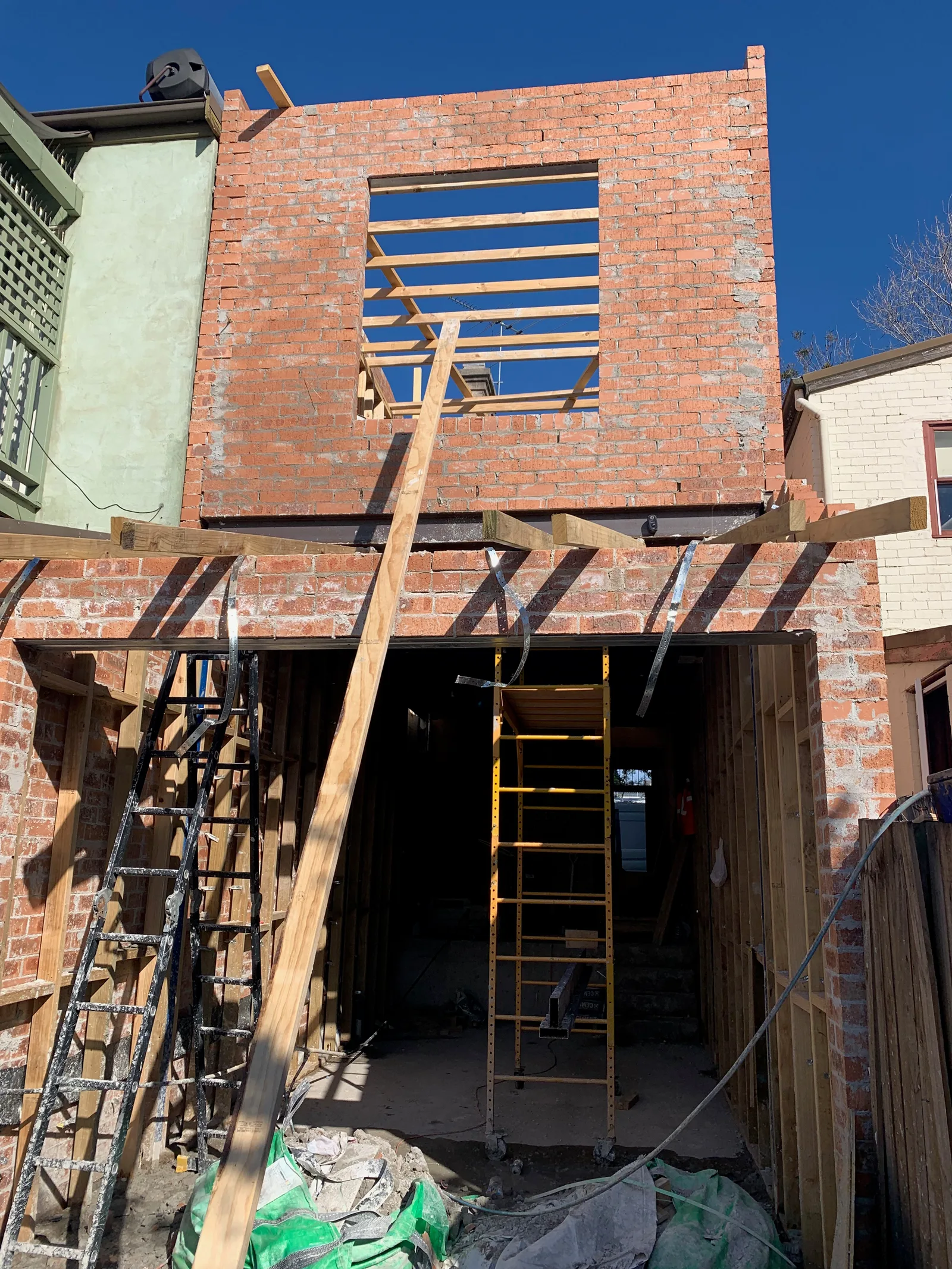 New brick walls built up two storeys against the original terrace's rear wall, with scaffolding and stacked bricks in the yard.
