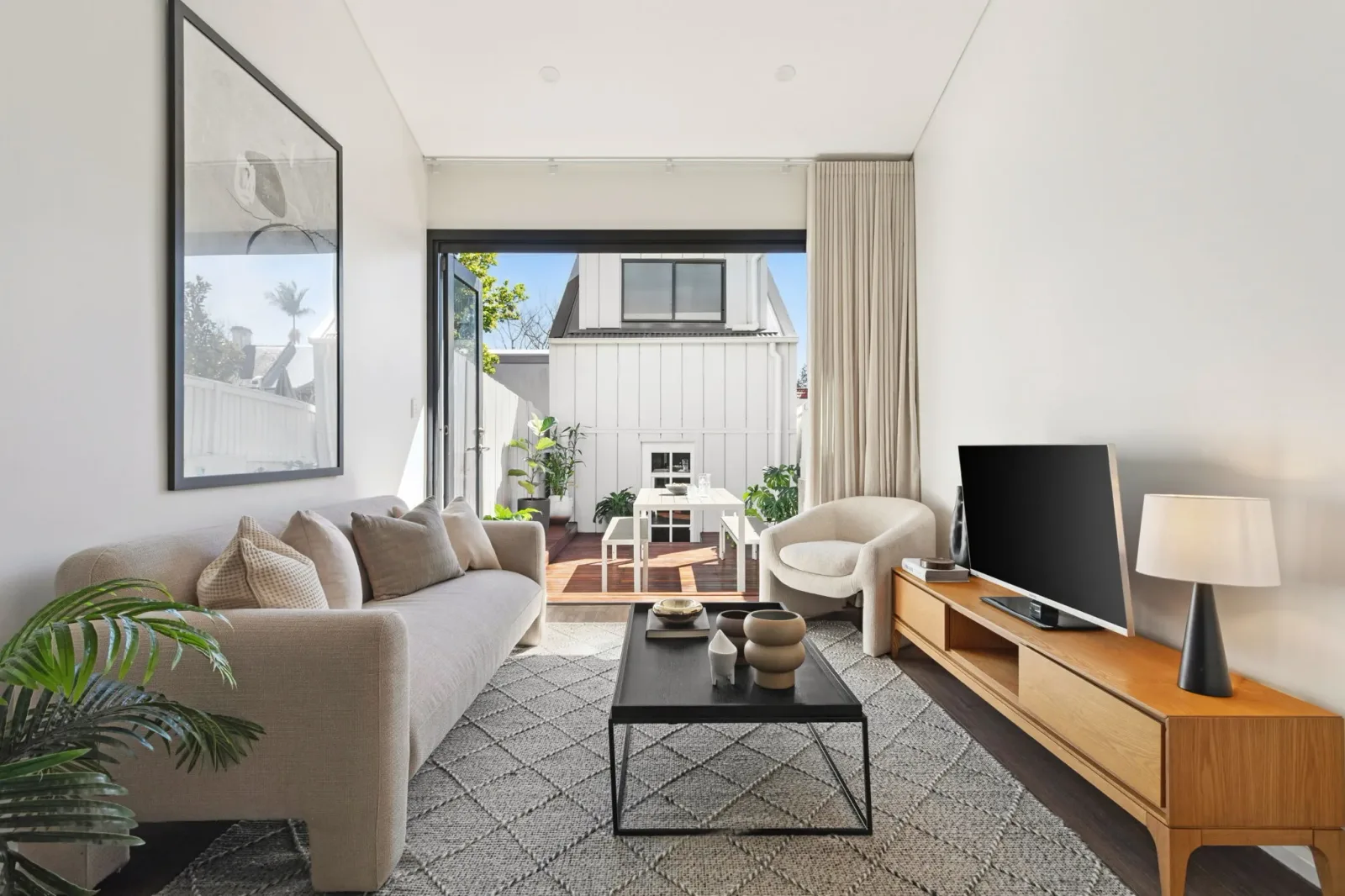 The living area, opening through full-height glazed doors to a timber deck, furnished with a linen sofa and a timber sideboard.