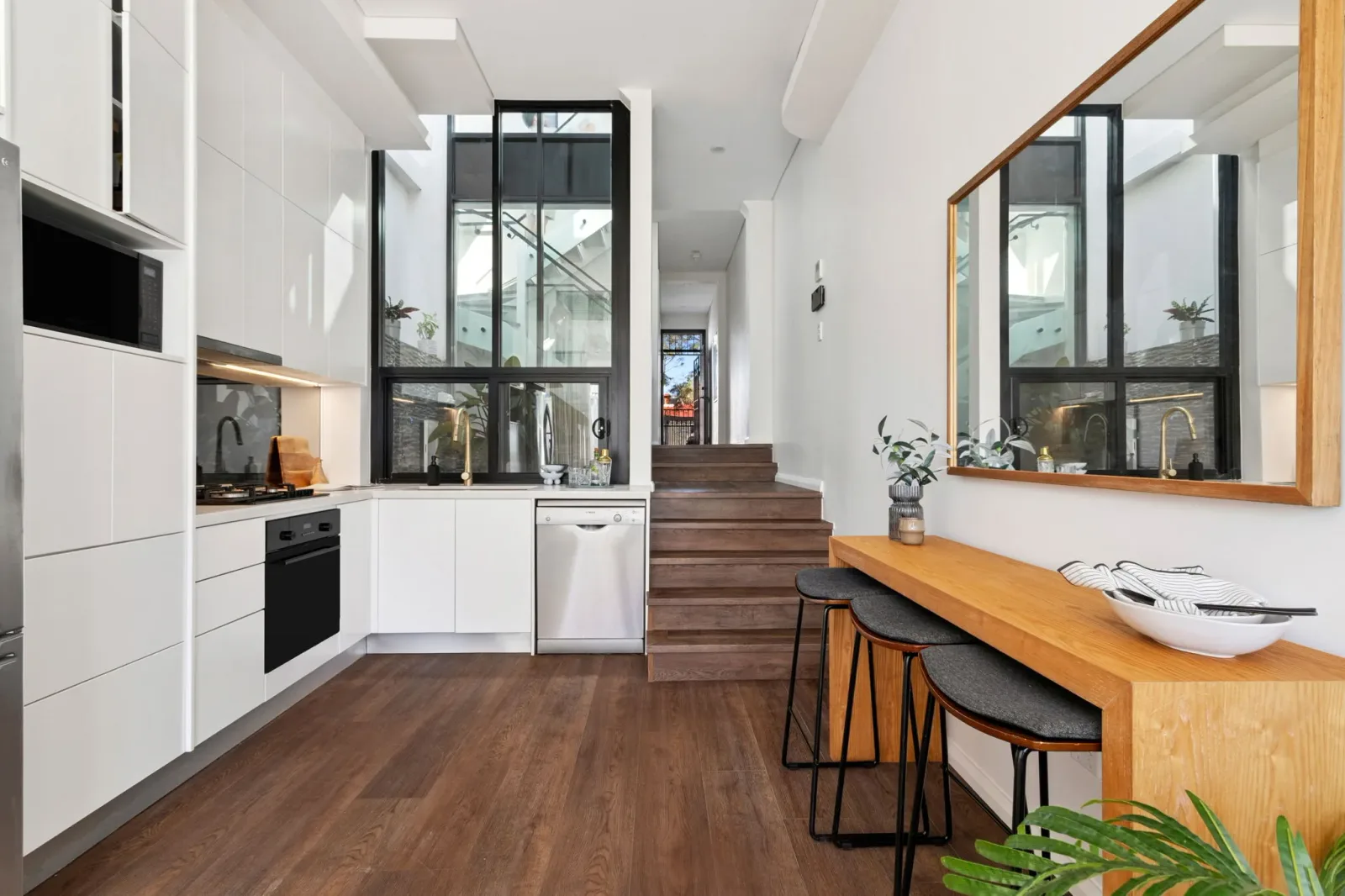 The kitchen, with white cabinetry, integrated appliances and a run of timber stairs beneath a skylight.