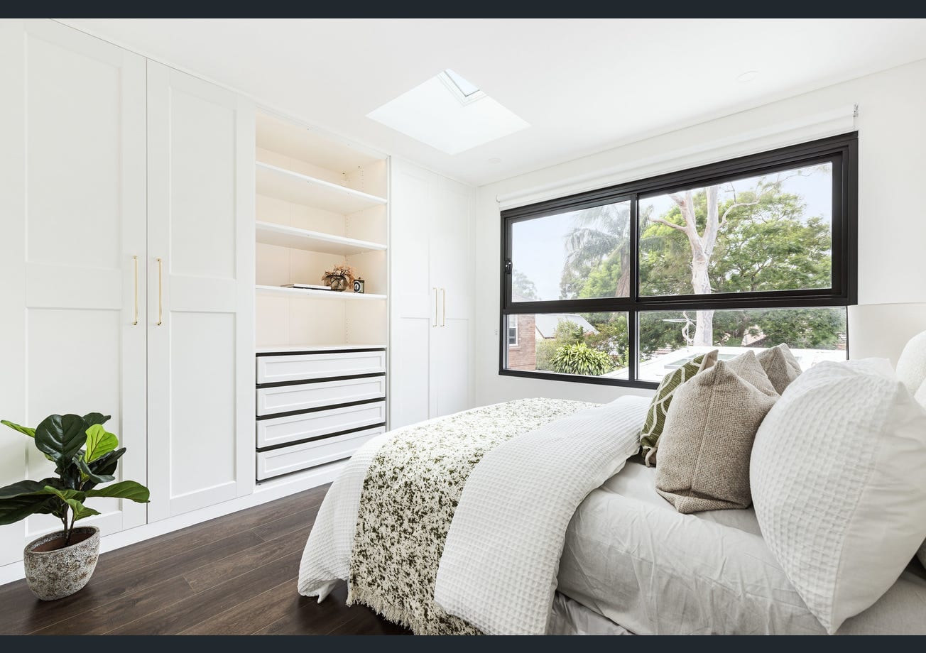 A finished bedroom with built-in wardrobes and shelving, and a skylight above the bed