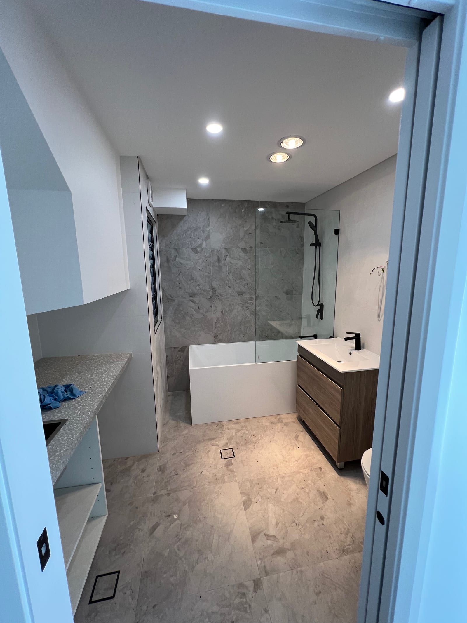 Before — The bathroom mid-fitout with tiling, bath and vanity installed but unstyled, and the same bathroom finished with a backlit mirror